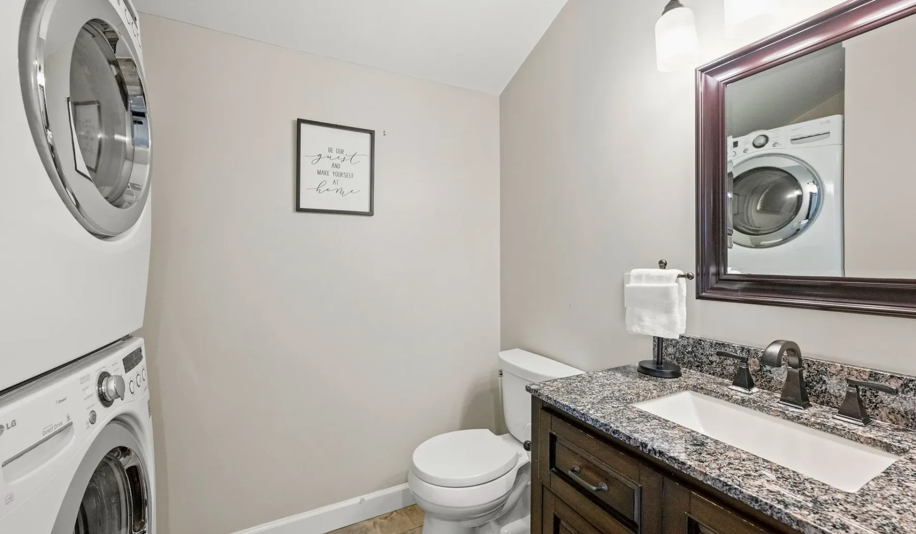 A bathroom with a sink, toilet, and stacked laundry machines.