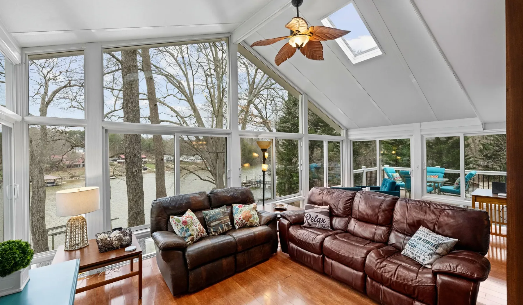 A sunroom with brown leather seating and large windows overlooking trees.