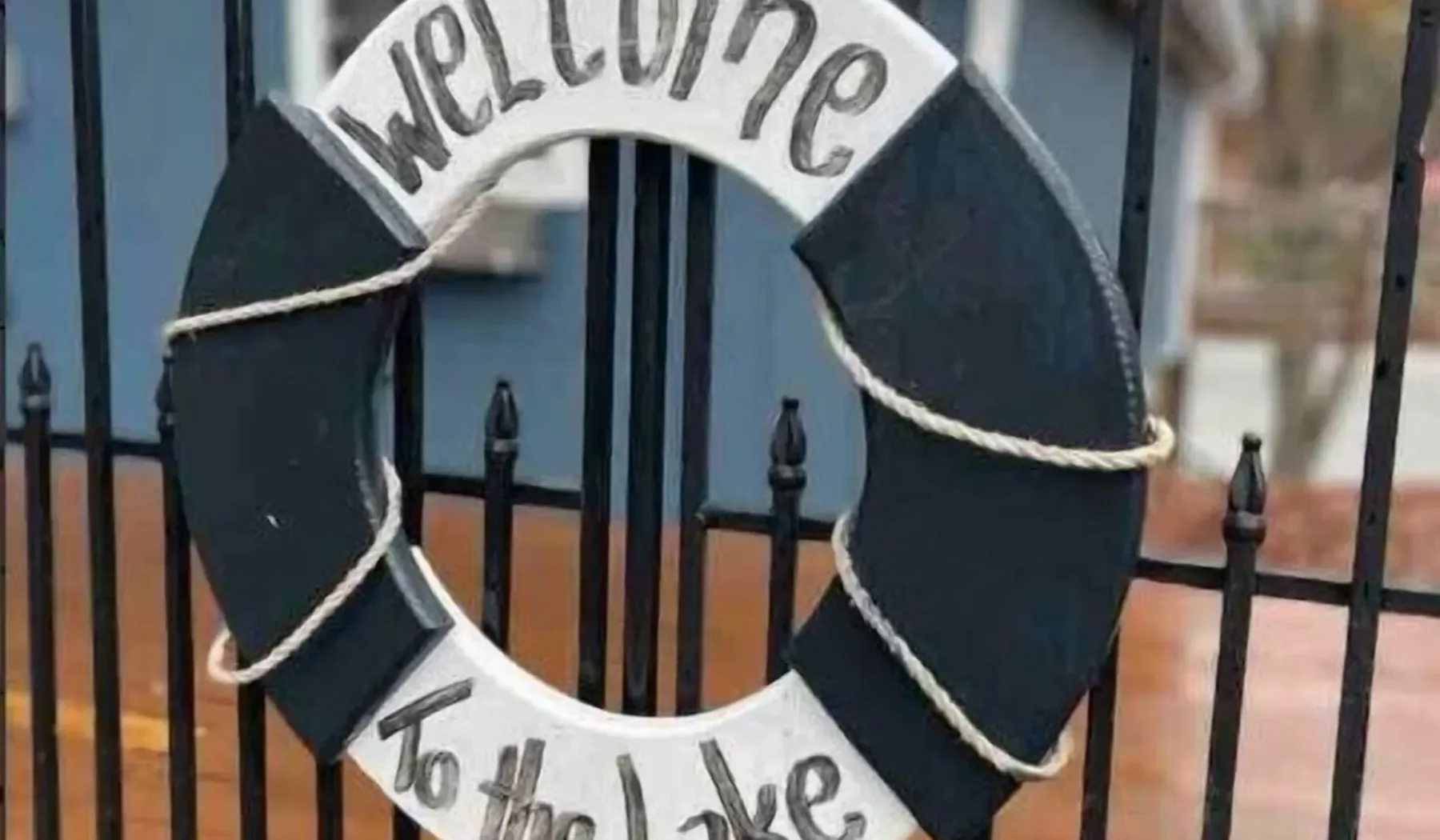 Un letrero de bienvenida con forma de salvavidas cuelga de una reja metálica negra.