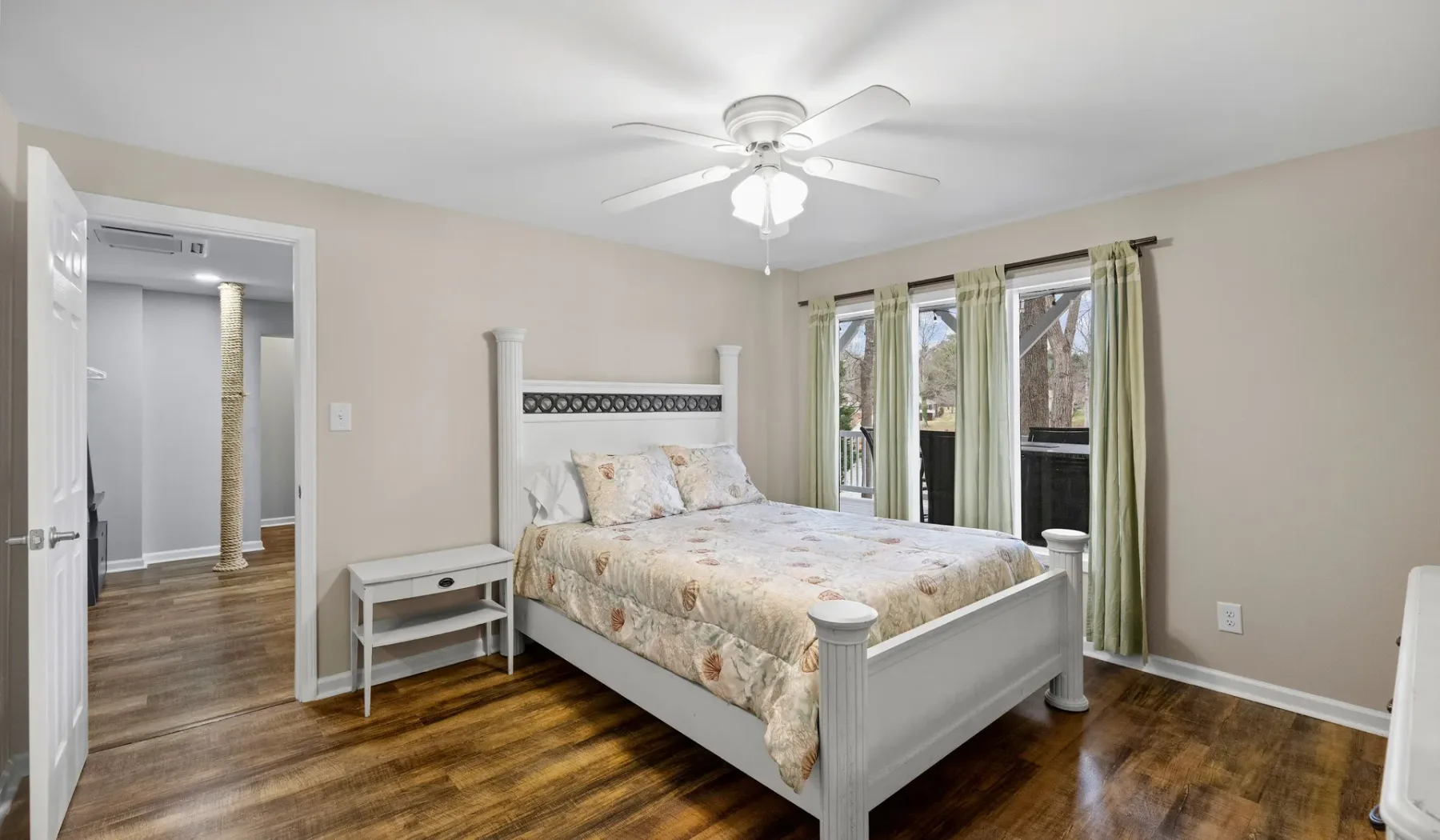 A bedroom with a white bed, bedside table, and windows with curtains.