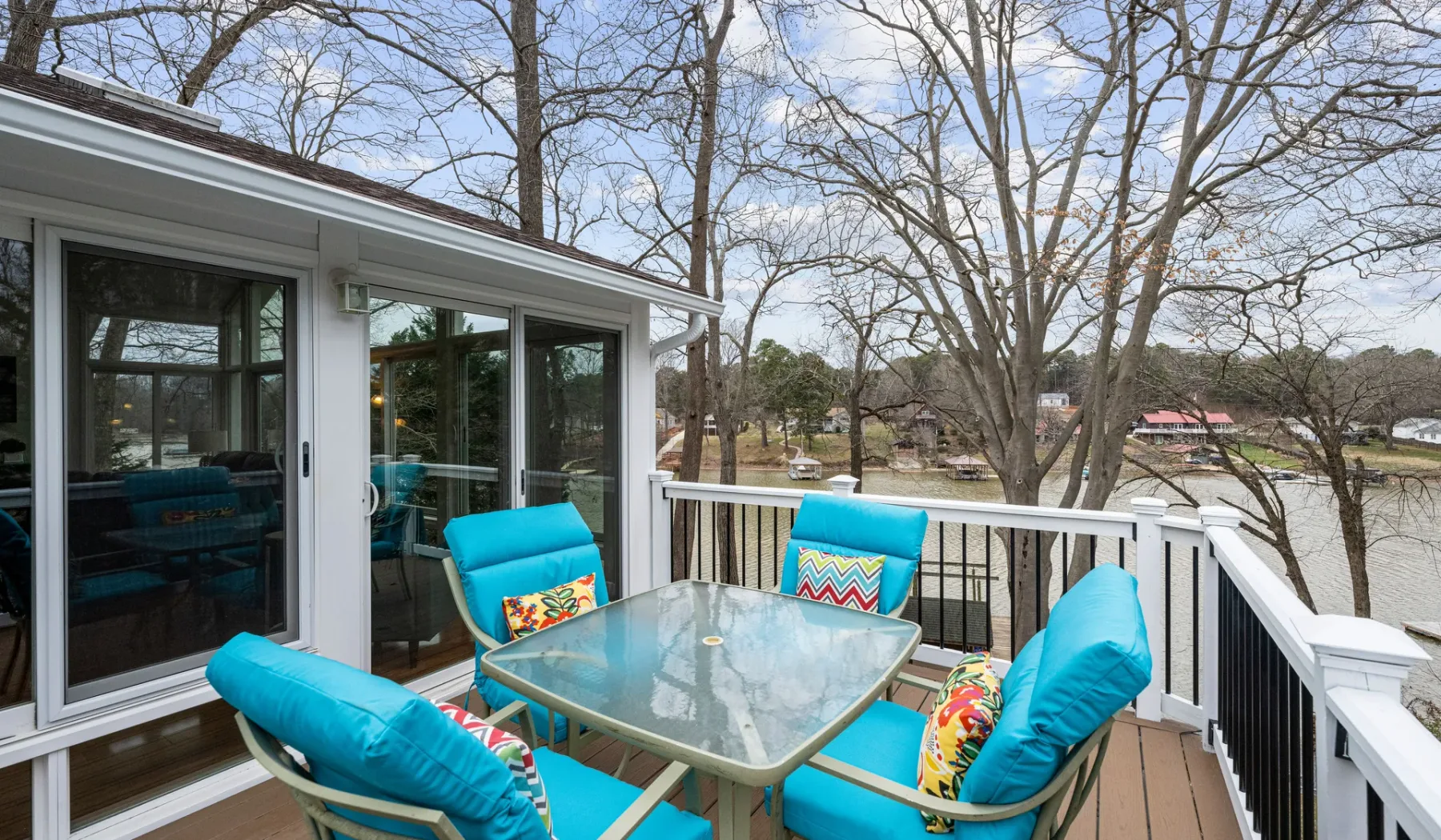 An outdoor deck with turquoise seating and a glass-top table overlooks trees.