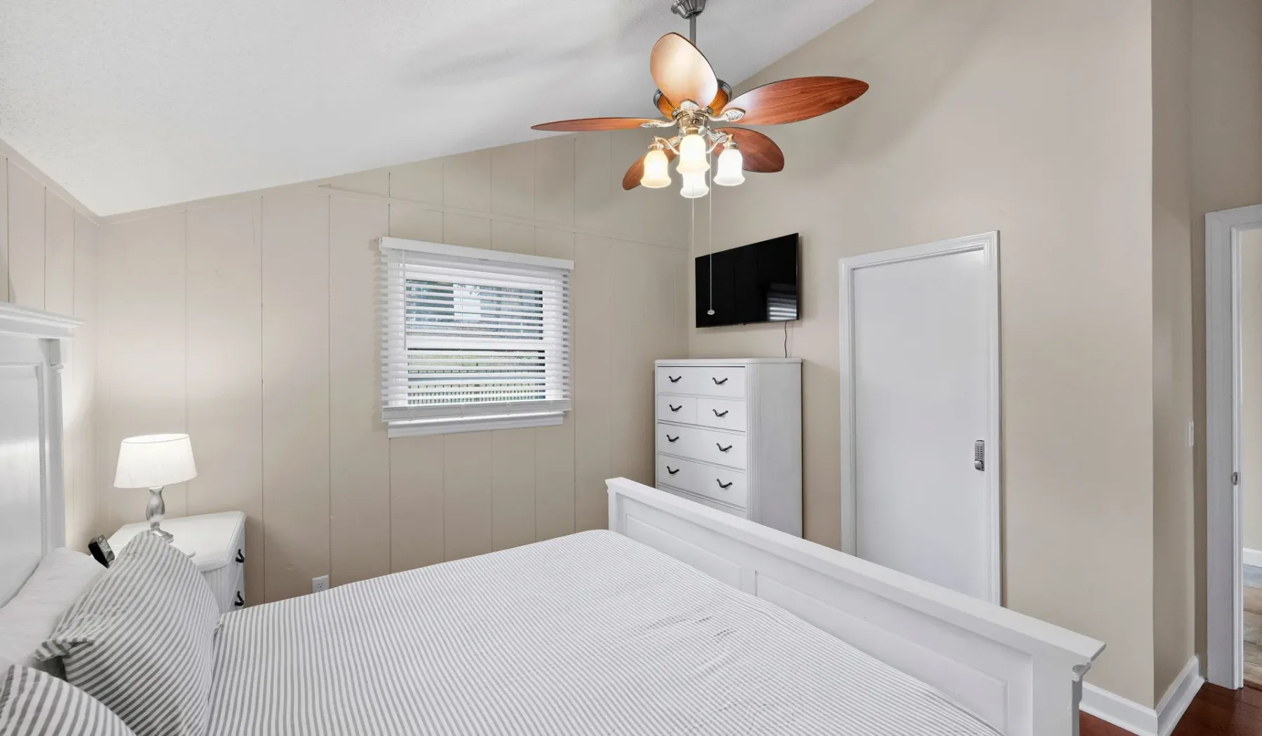 A bright bedroom with a bed, dresser, and ceiling fan.