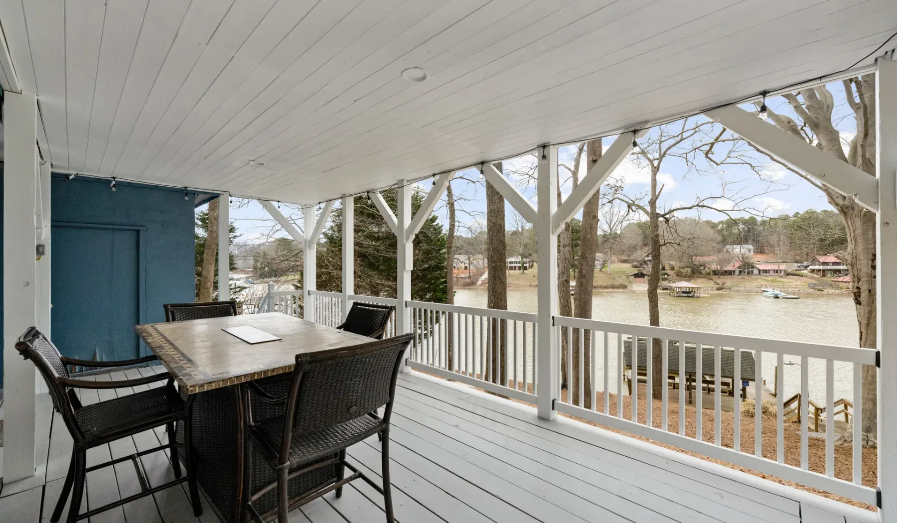 A covered deck overlooks a waterfront, with outdoor seating and a dining table.