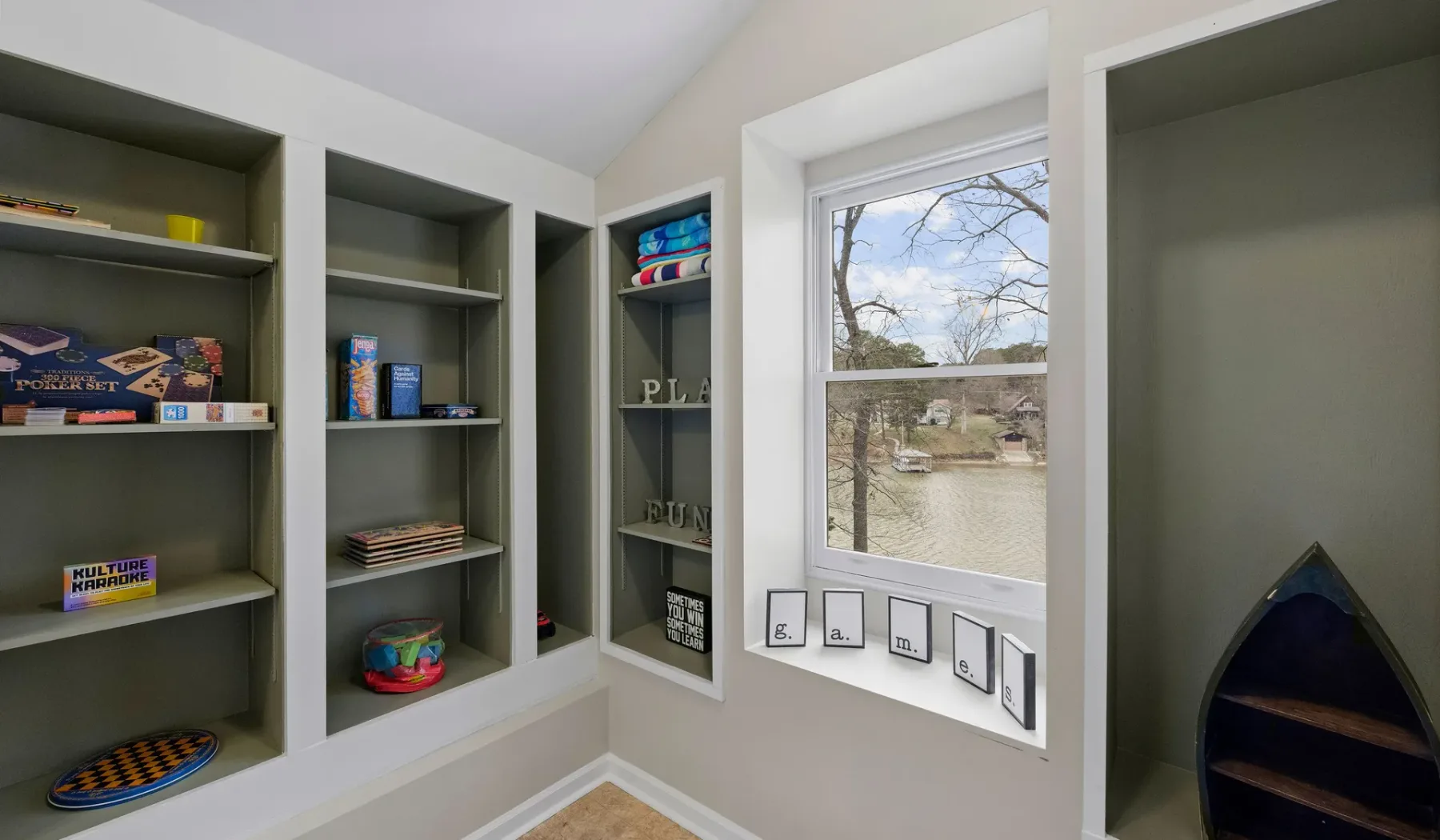 A built-in shelving nook surrounds a window overlooking a tree-lined pond.