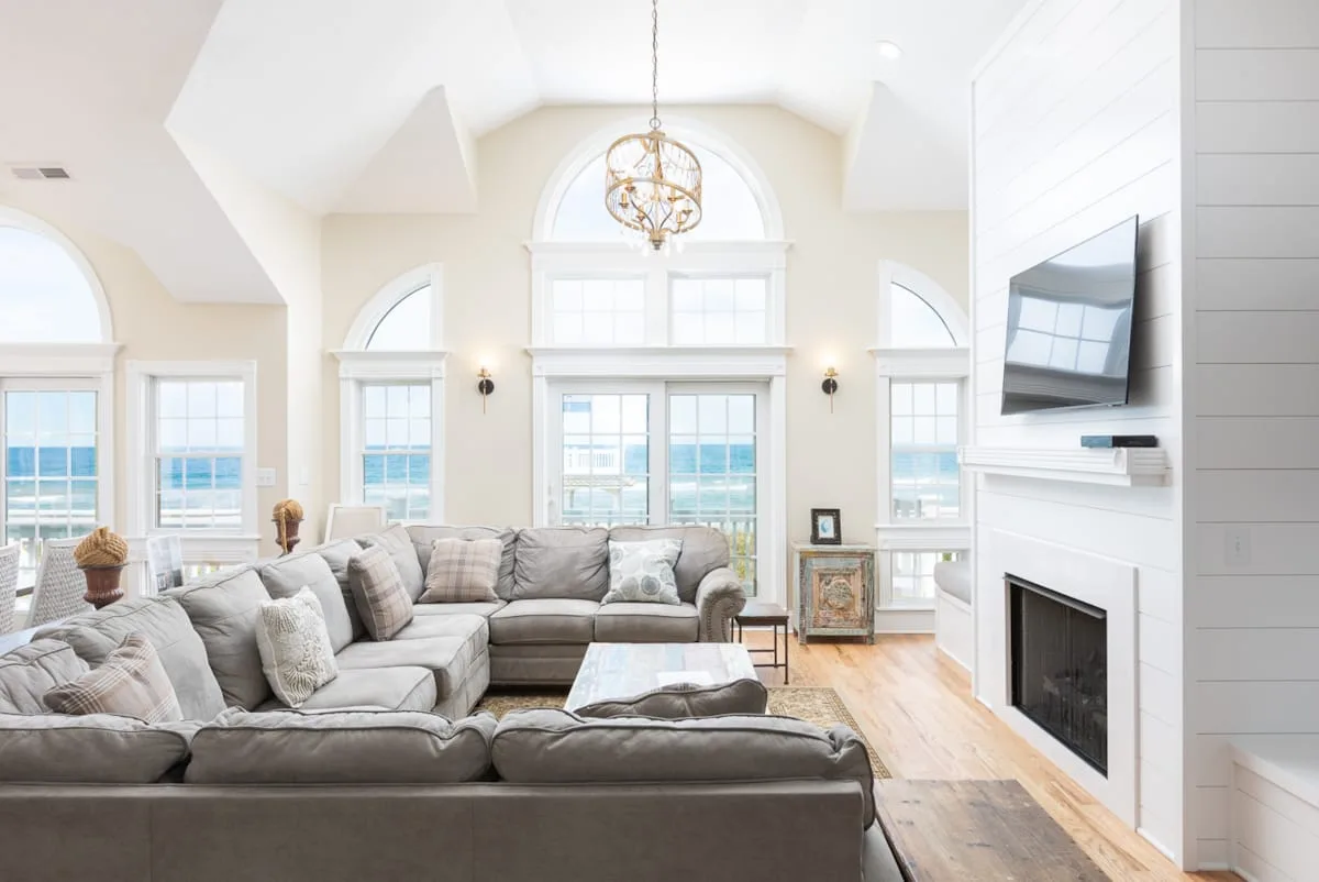 A bright living room with gray seating, large windows, and a fireplace.