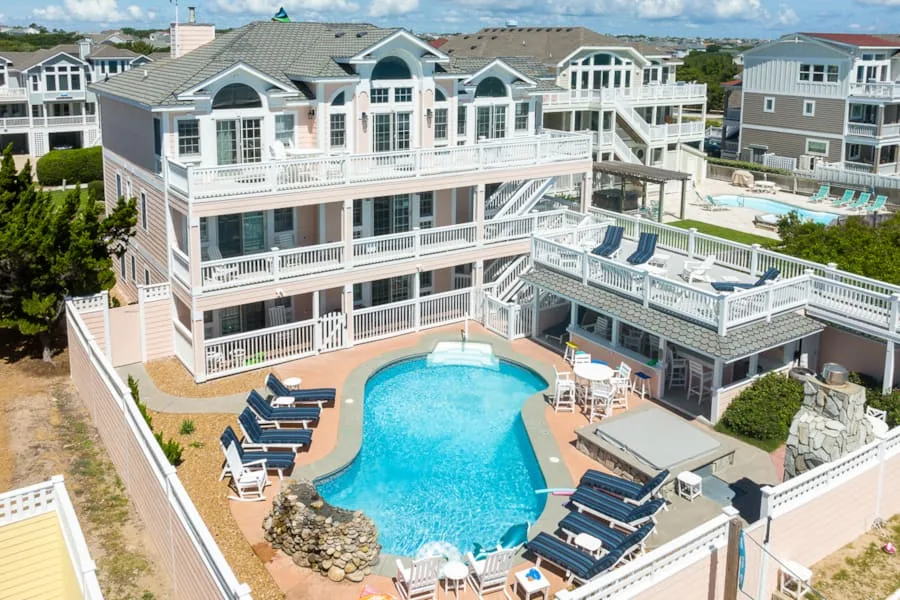 A large multi-story house overlooks an outdoor swimming pool and deck.