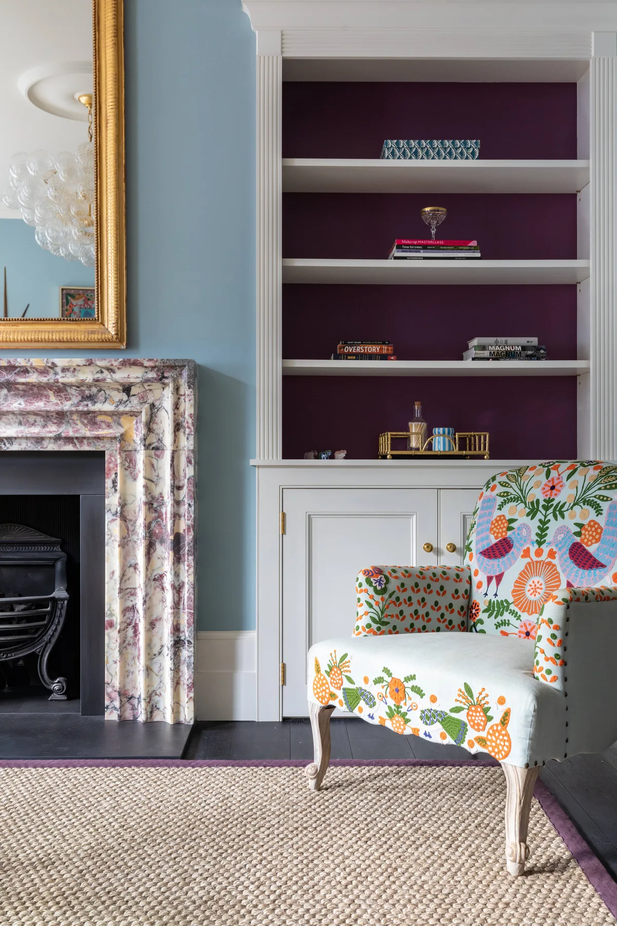 Una zona de estar con un sillón estampado junto a una chimenea y estantes empotrados.