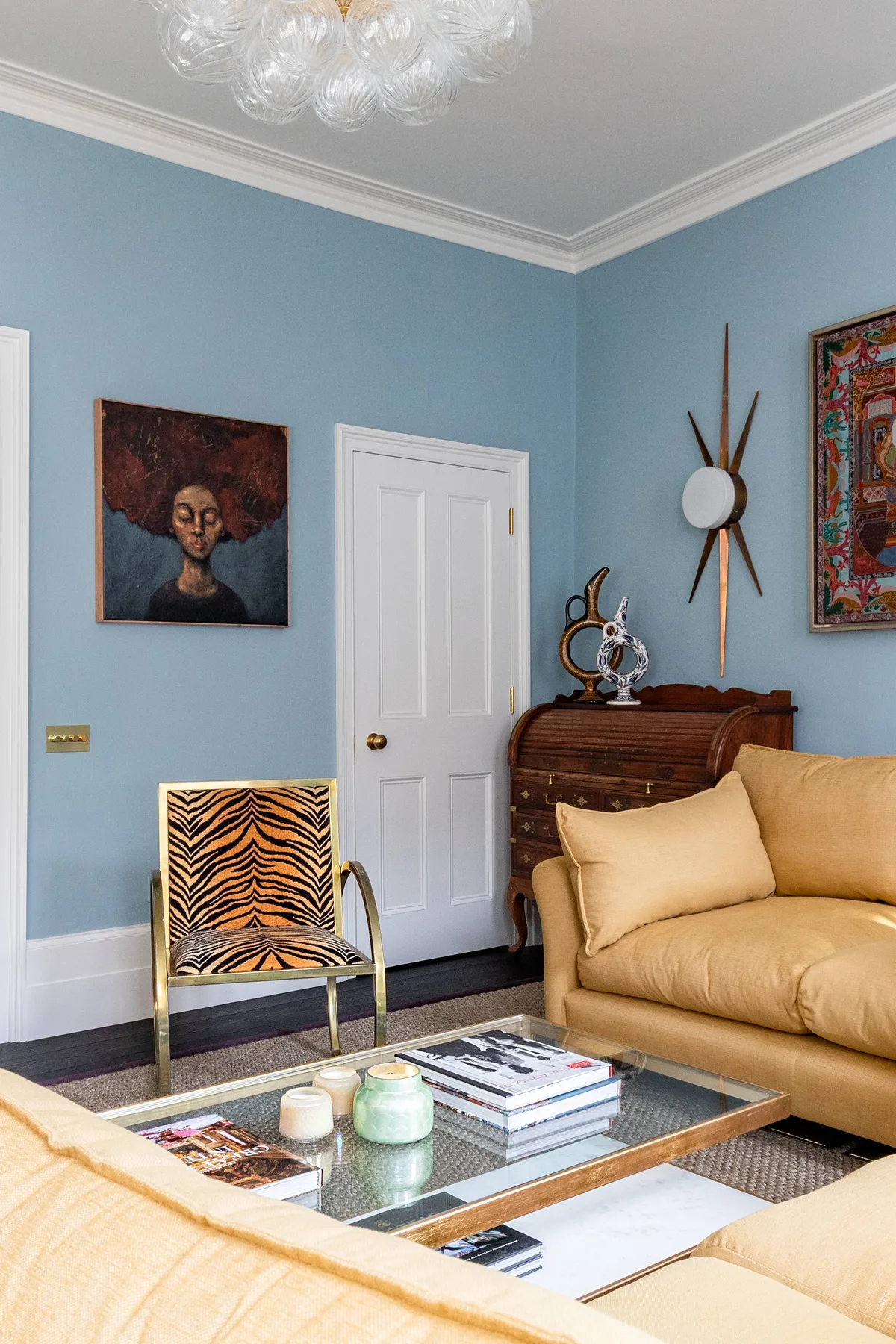 Una sala de estar con paredes azules, cuadros, asientos y una mesa de centro de vidrio.