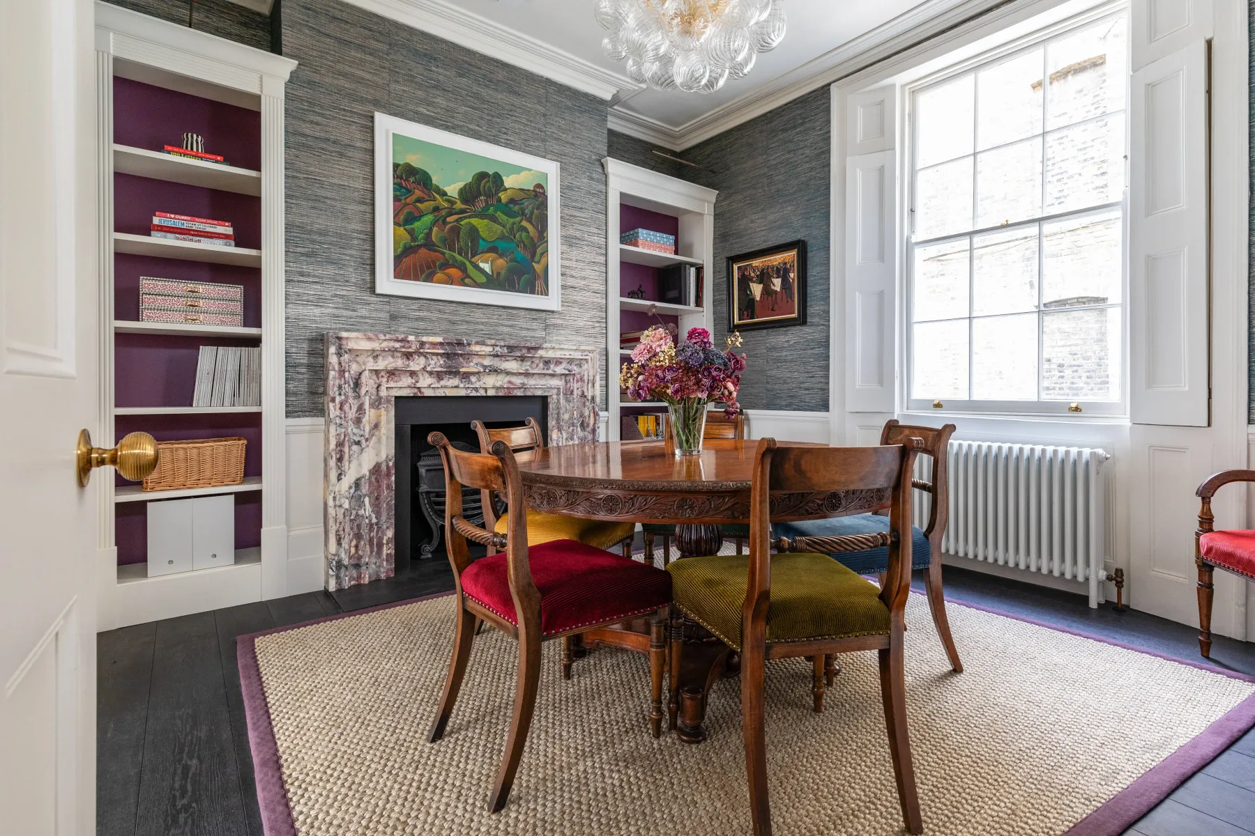 Comedor con mesa de madera, sillas de colores y una ventana grande.