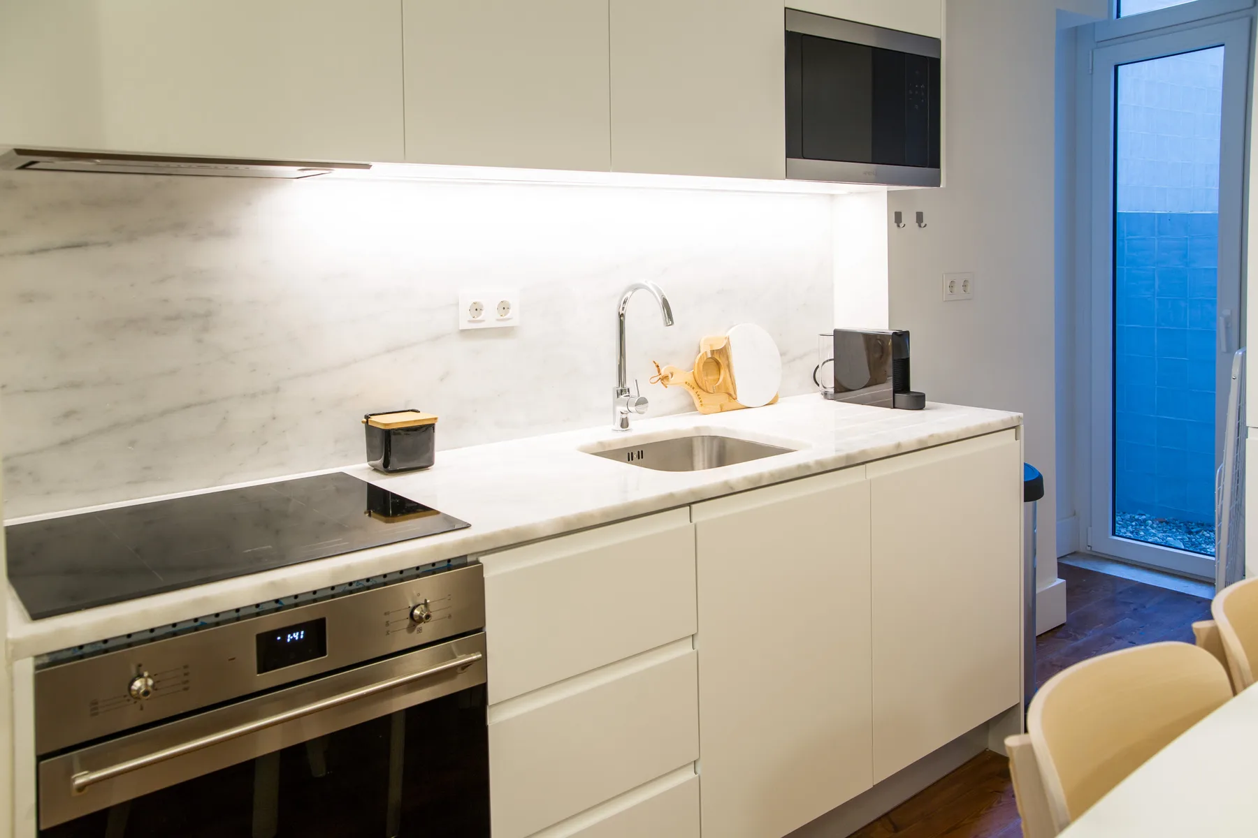 A bright kitchen with a built-in oven, cooktop, and counter beside a glass door.