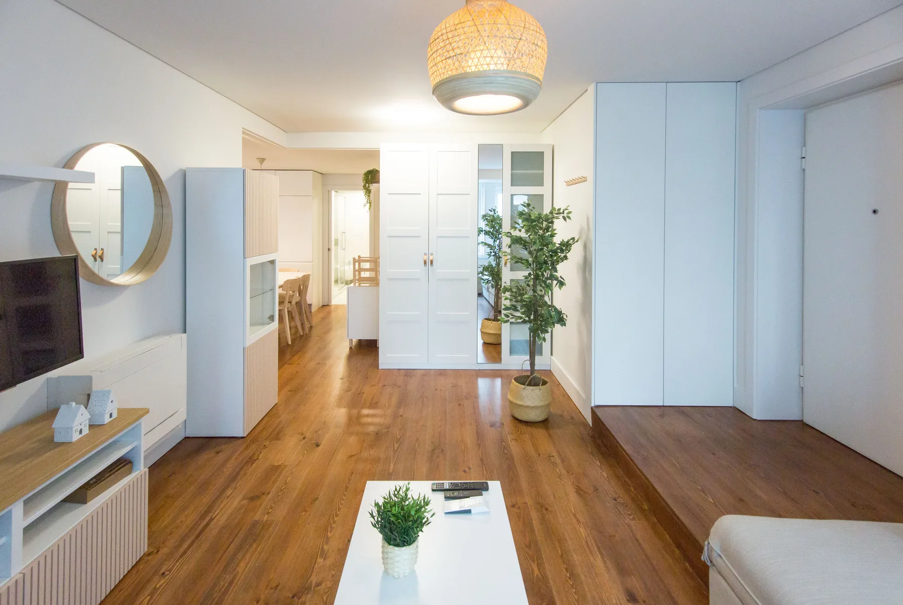 A bright living room with wood flooring, a television, and a potted plant.