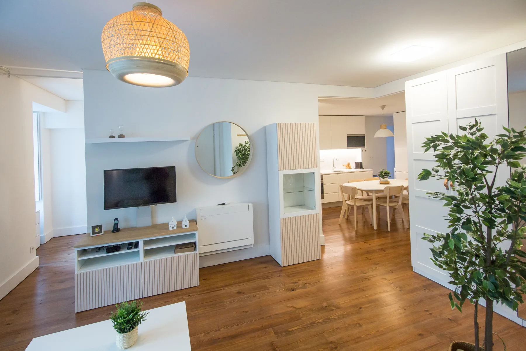 A bright living room opens into a dining area with a television and wooden flooring.