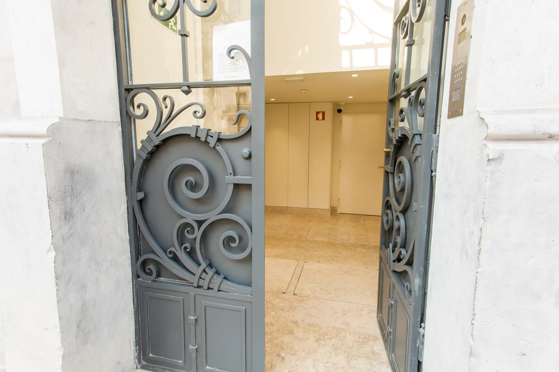 An open ornate metal doorway leads into a bright interior hallway.
