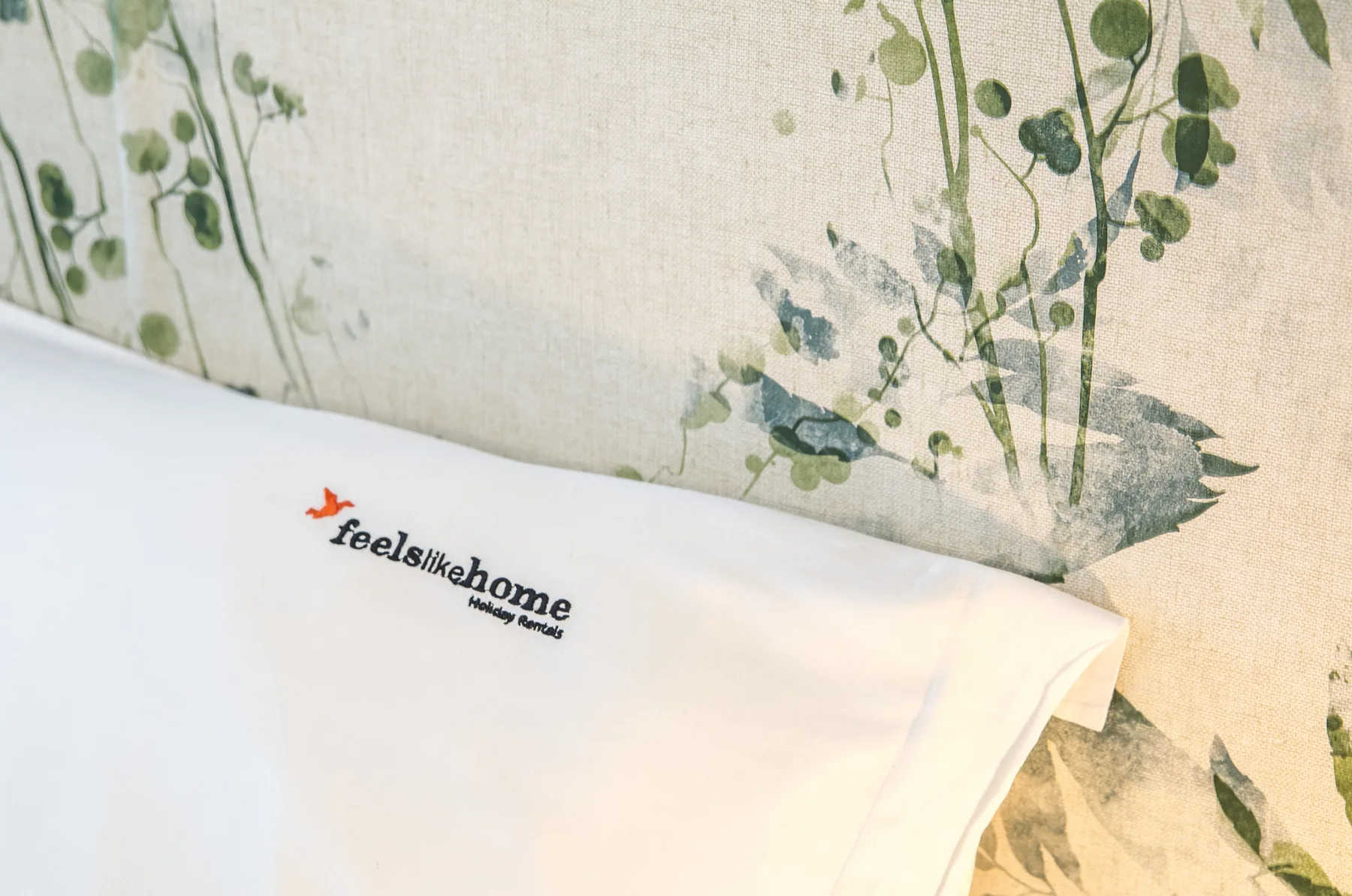 A white bed with a printed logo rests against botanical-patterned bedding.
