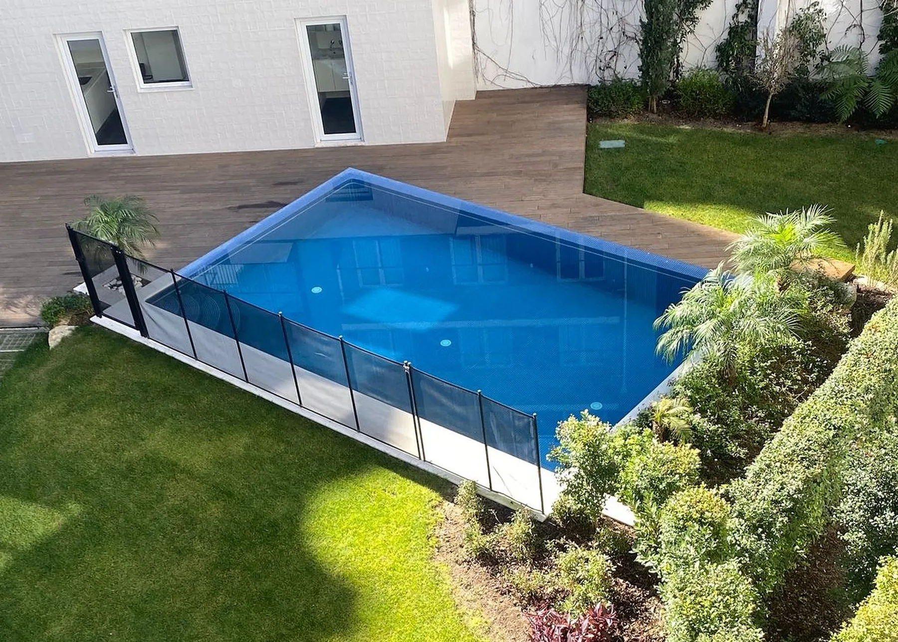 An outdoor swimming pool bordered by a wooden deck and green lawn.