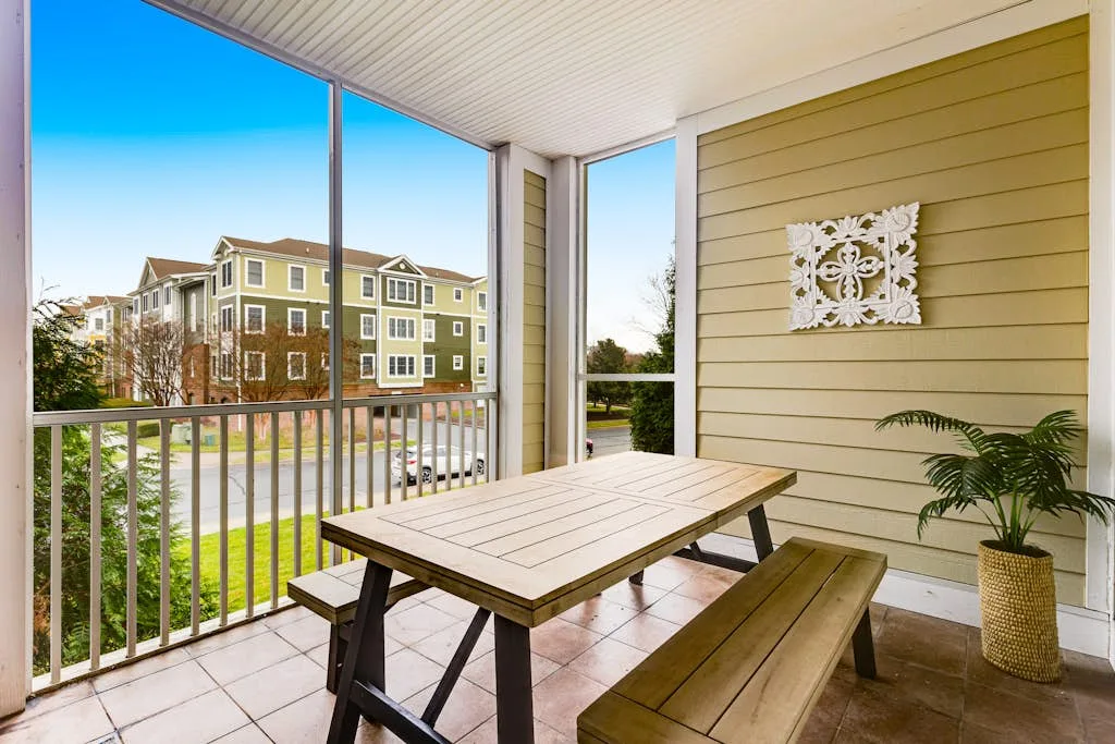 A covered outdoor patio with a wooden picnic table and a potted plant.