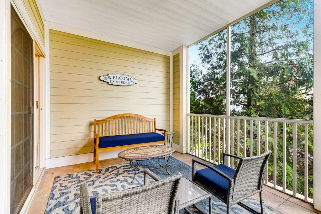 A covered balcony seating area with a bench, chairs, and leafy trees outside.