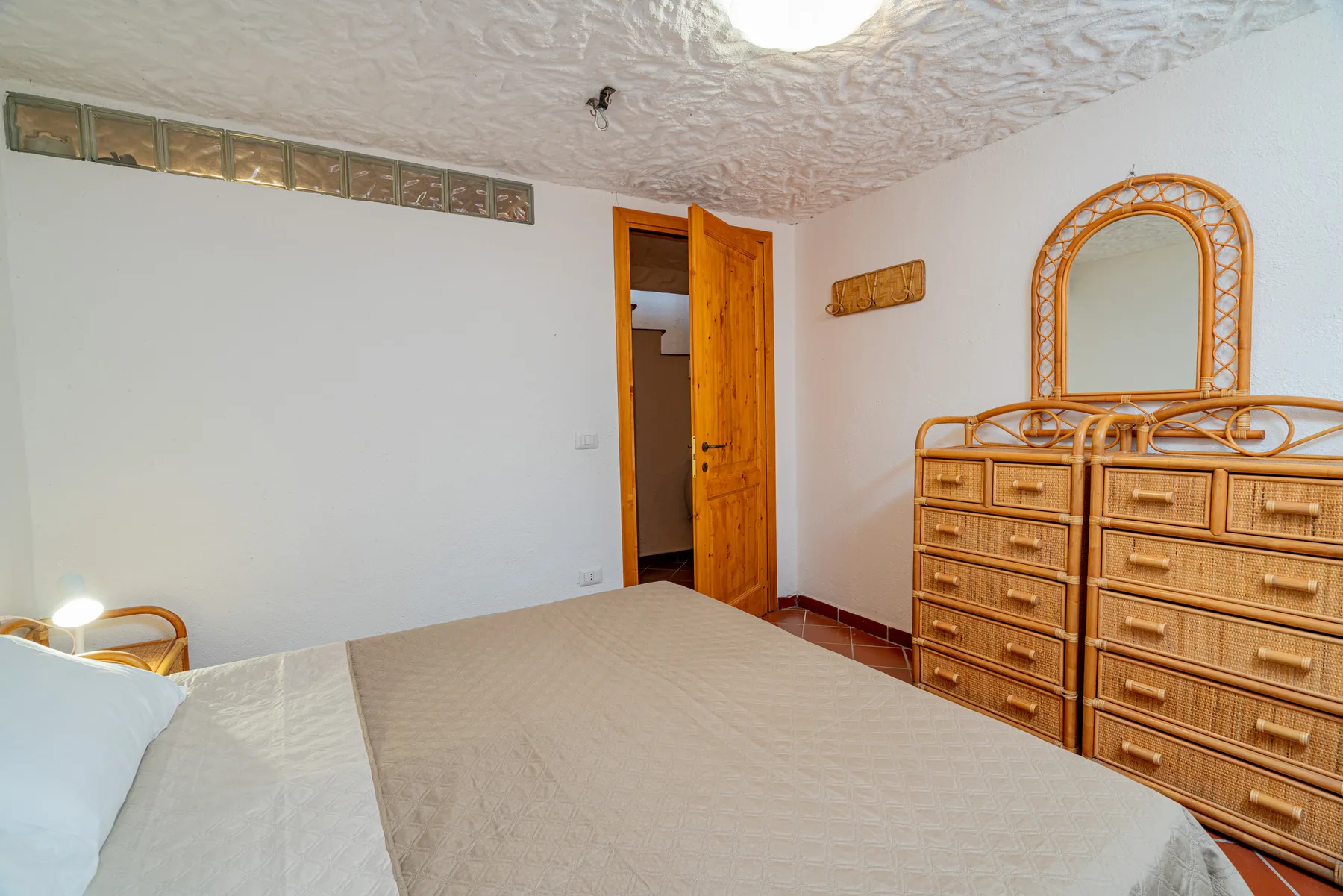 Un dormitorio con una cama y una cómoda de mimbre bajo un espejo arqueado.