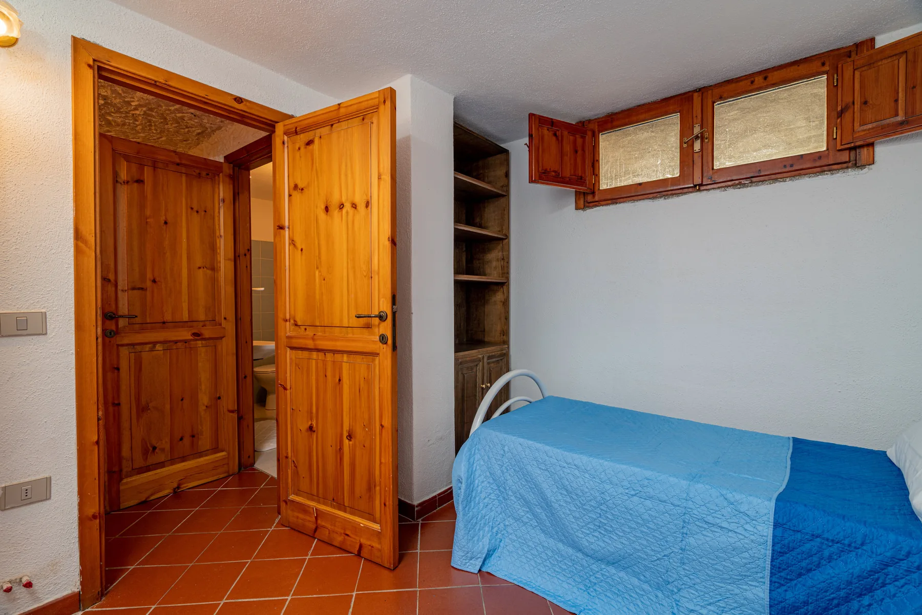 Dormitorio con una cama cubierta de azul y puertas de madera abiertas.