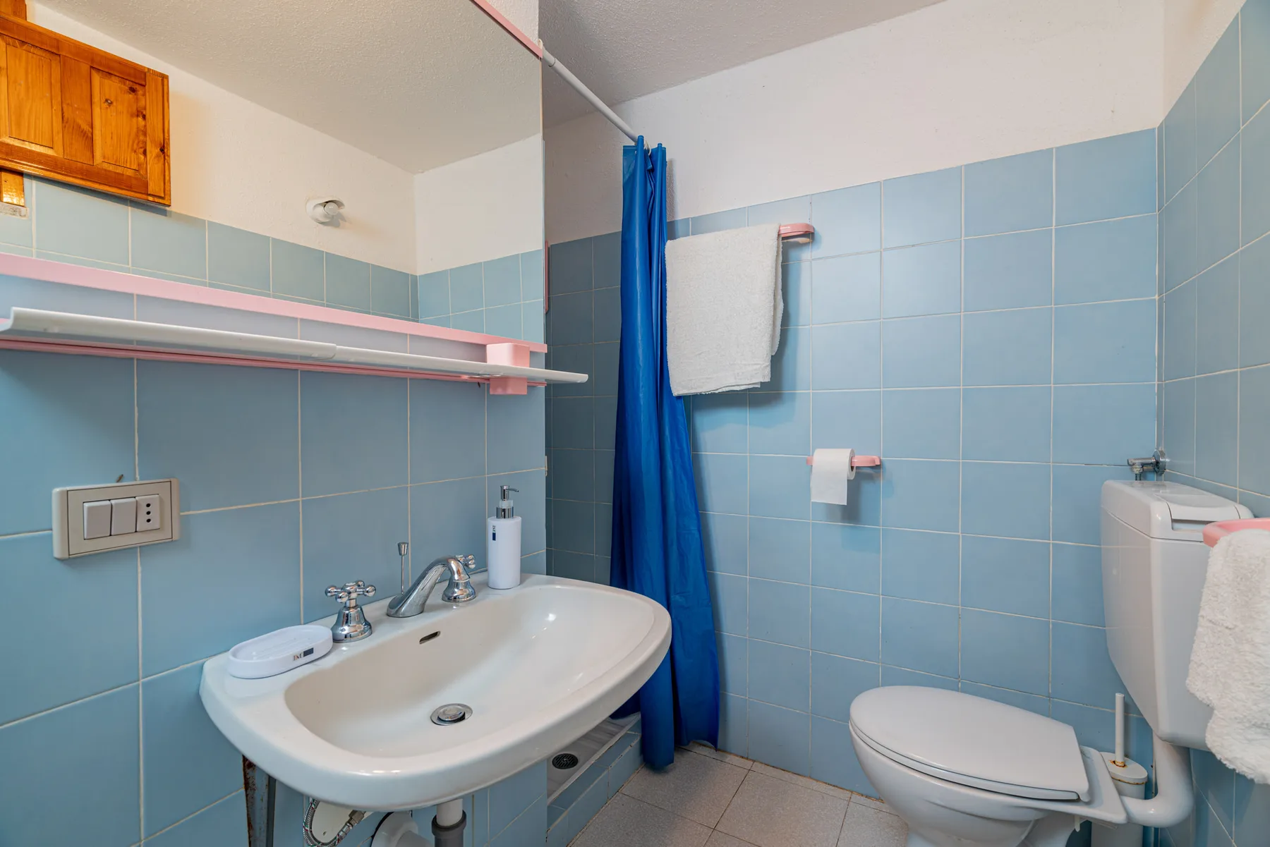 Un baño alicatado con lavabo, inodoro y cortina de ducha azul.