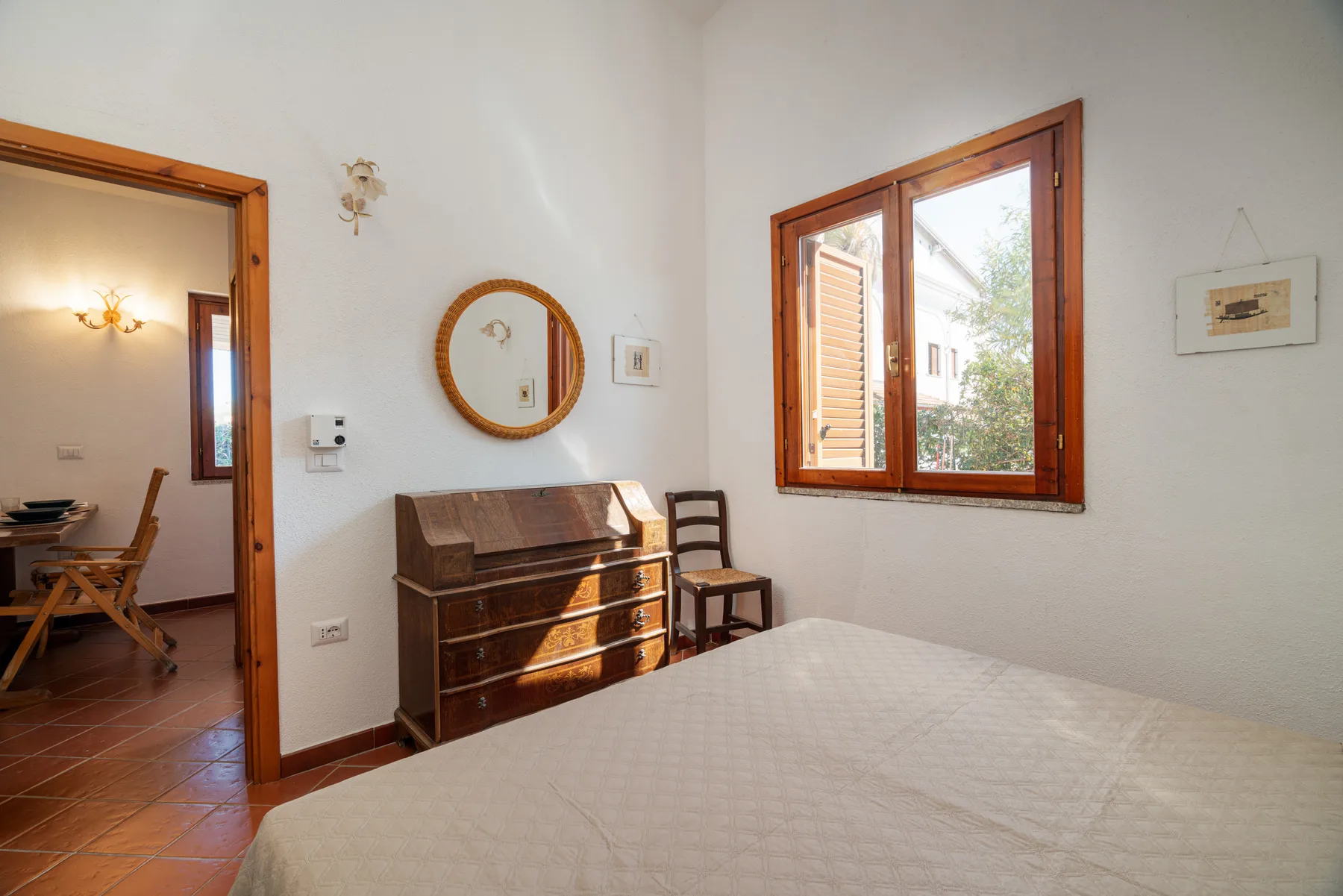 Un dormitorio con una cómoda de madera, un espejo de pared y una ventana con vista a edificios.