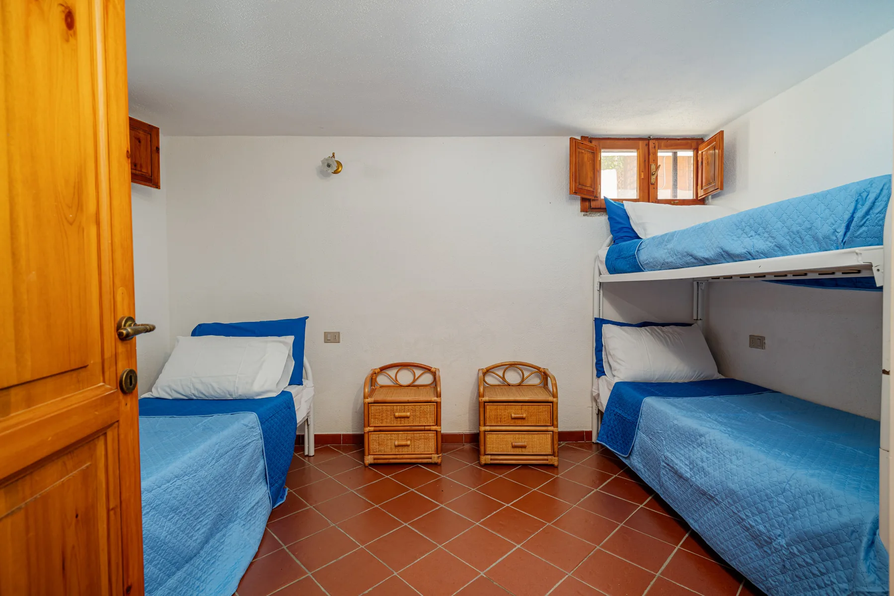 Dormitorio con ropa de cama azul y una litera junto a una cama individual.