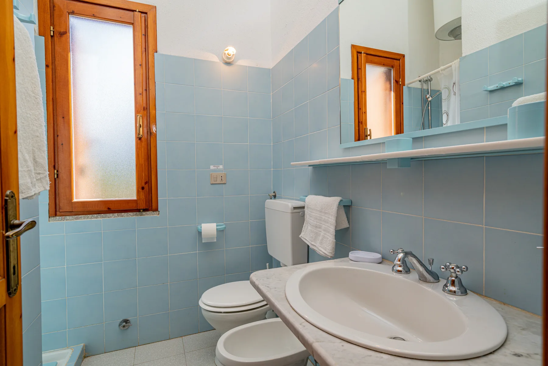 Un baño con azulejos, lavabo, inodoro y una ventana translúcida.
