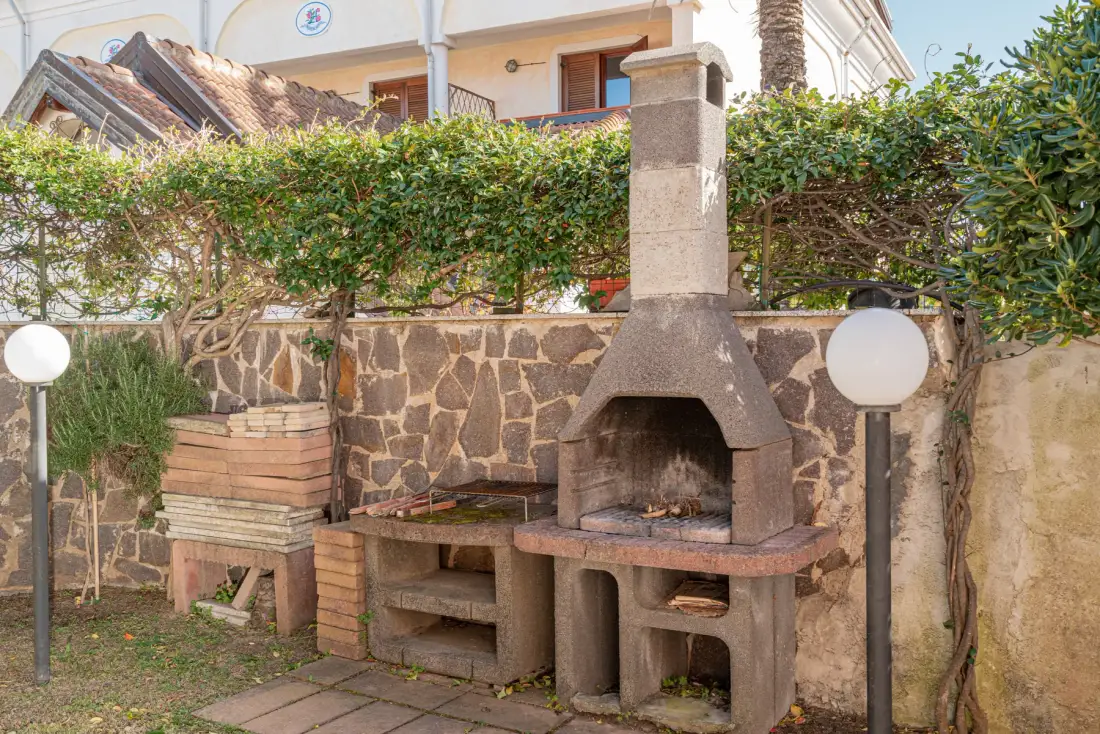Una barbacoa exterior de obra está junto a un muro de piedra bajo un seto recortado.