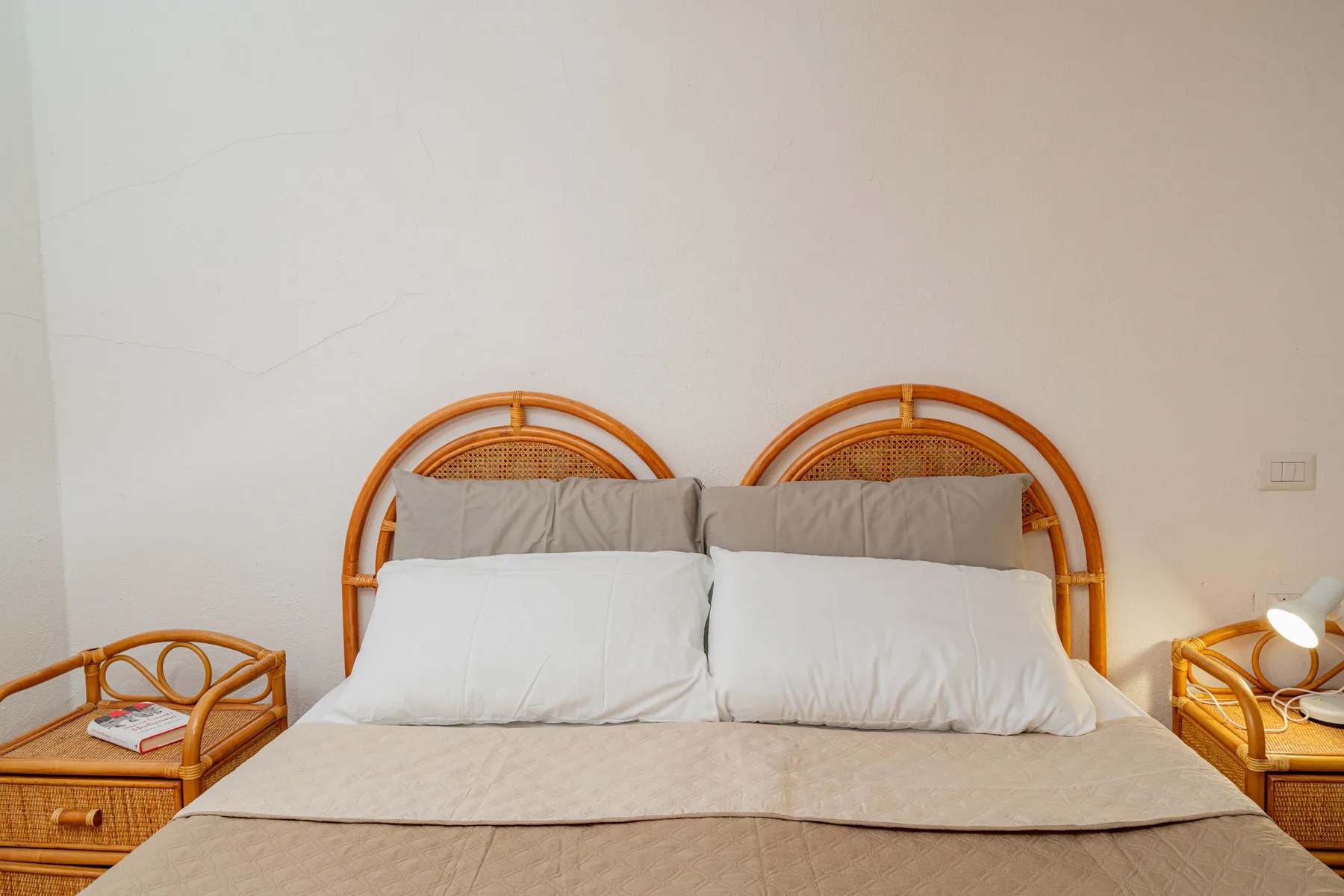 Dormitorio con una cama y un cabecero curvo de madera frente a una pared clara.