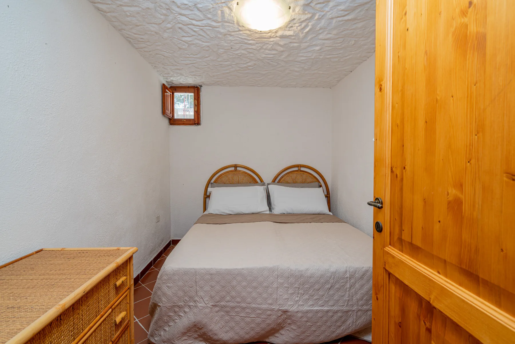 Un dormitorio con una cama doble, una ventana pequeña y una puerta de madera abierta.