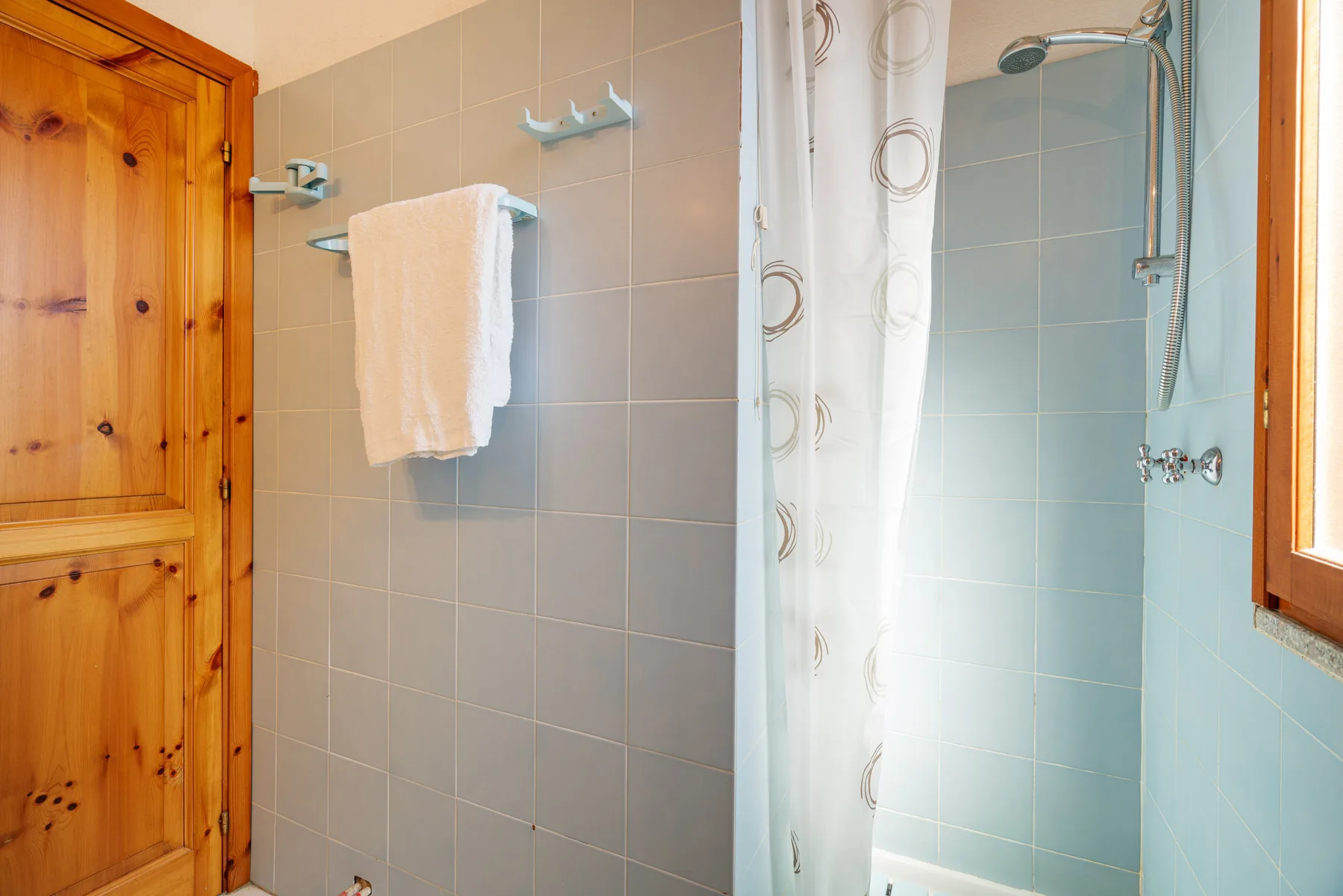 Un baño de azulejos con ducha y una toalla colgada en la pared.
