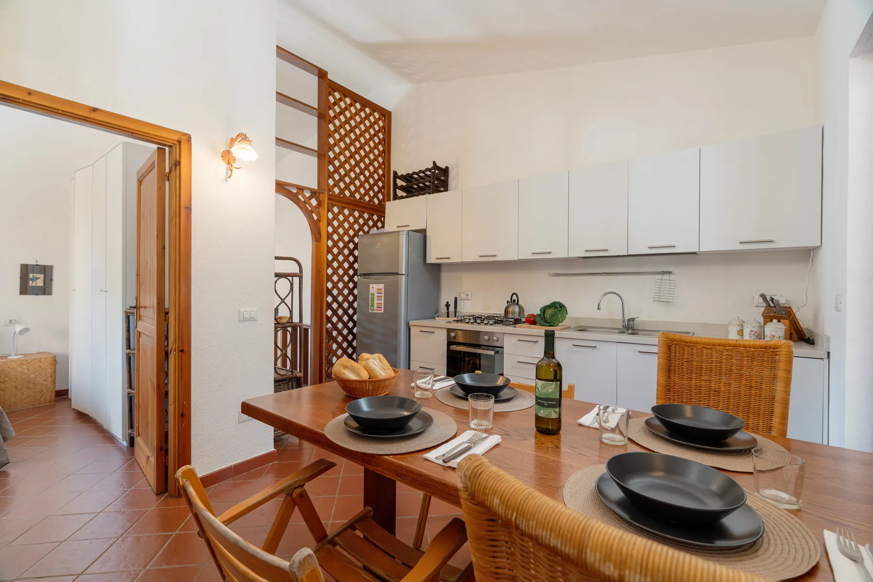 Una mesa está preparada frente a una cocina luminosa con armarios blancos.