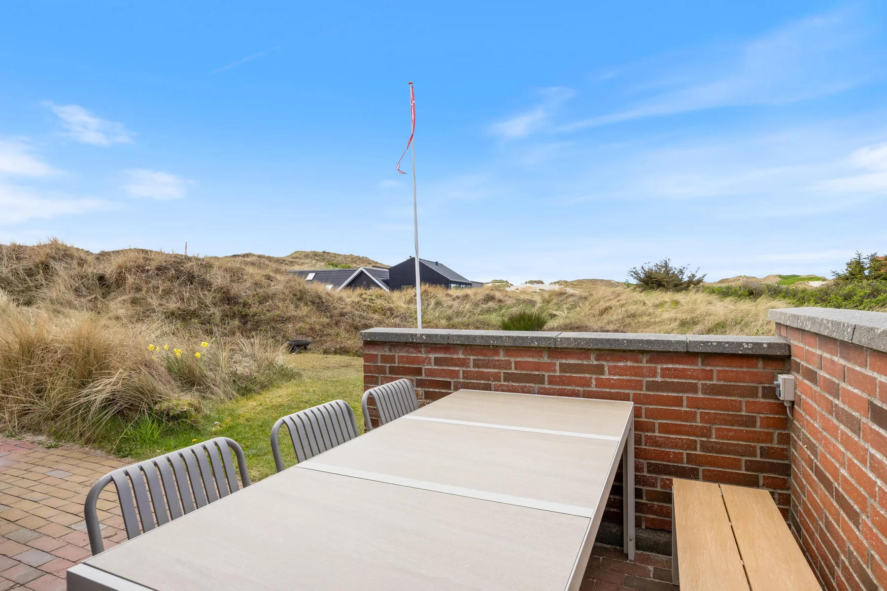 An outdoor patio with a dining table overlooks grassy dunes.