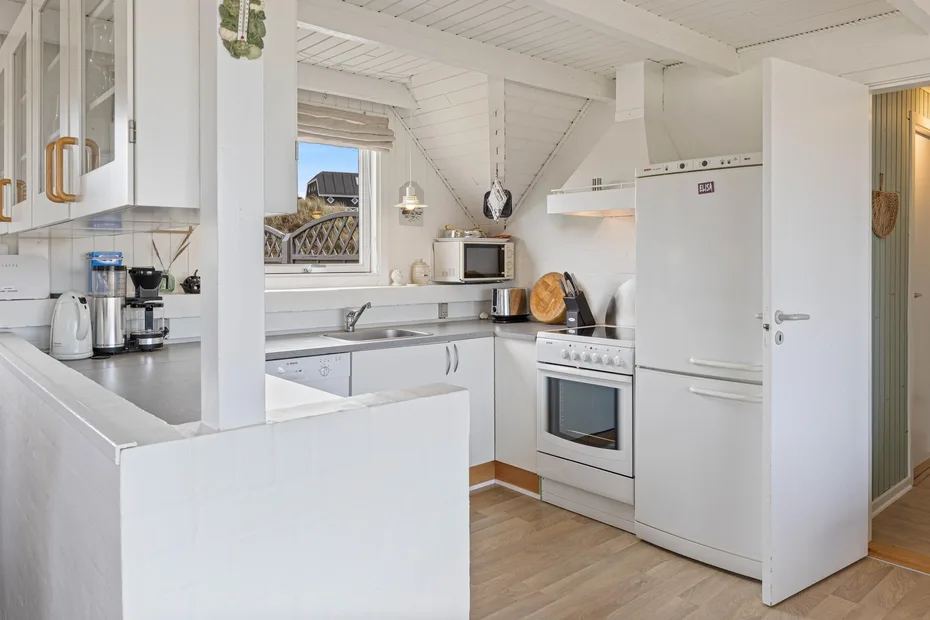 A bright kitchen with white cabinets, counters, and a freestanding refrigerator.