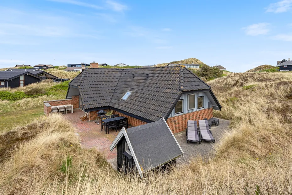 A brick house with a dark tiled roof sits among grassy dunes.
