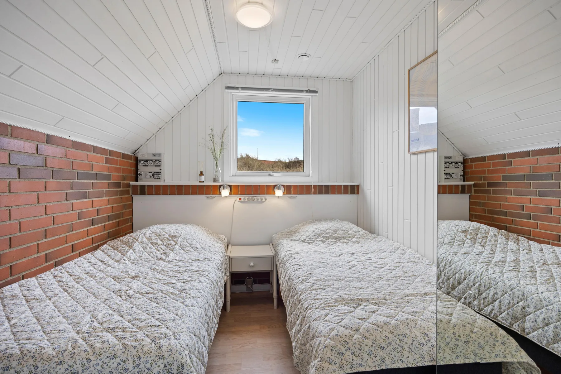 A bedroom with two single beds beneath a sloped ceiling and a window.
