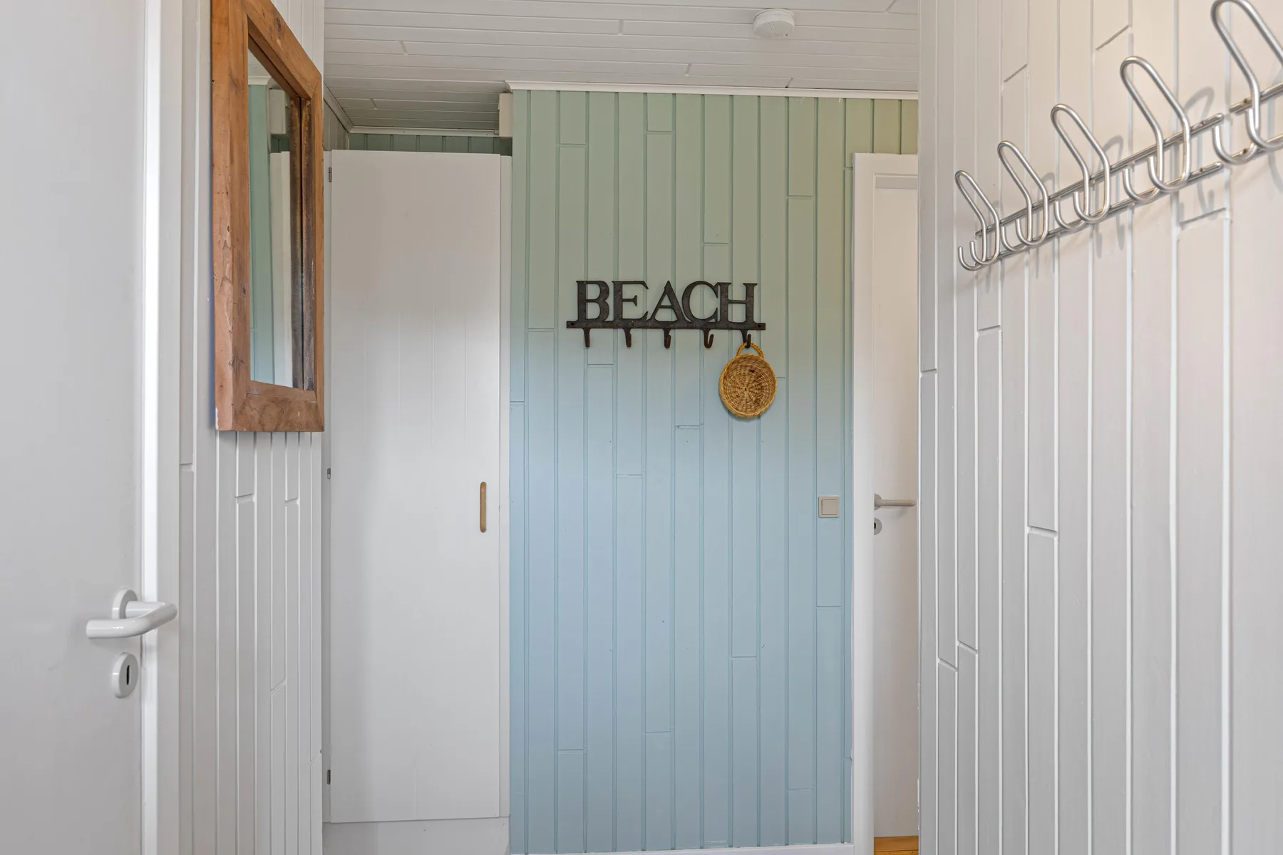 A hallway with pale blue paneled walls and coat hooks.