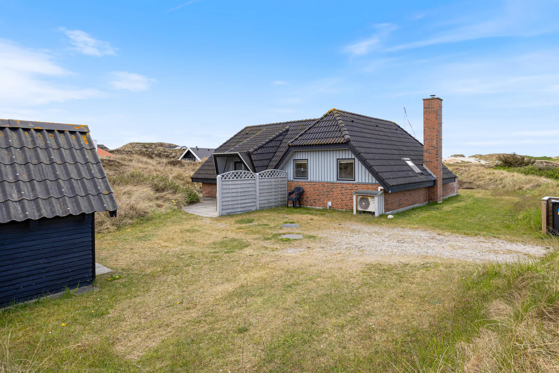 A low house with a dark tiled roof stands in a grassy dune landscape.