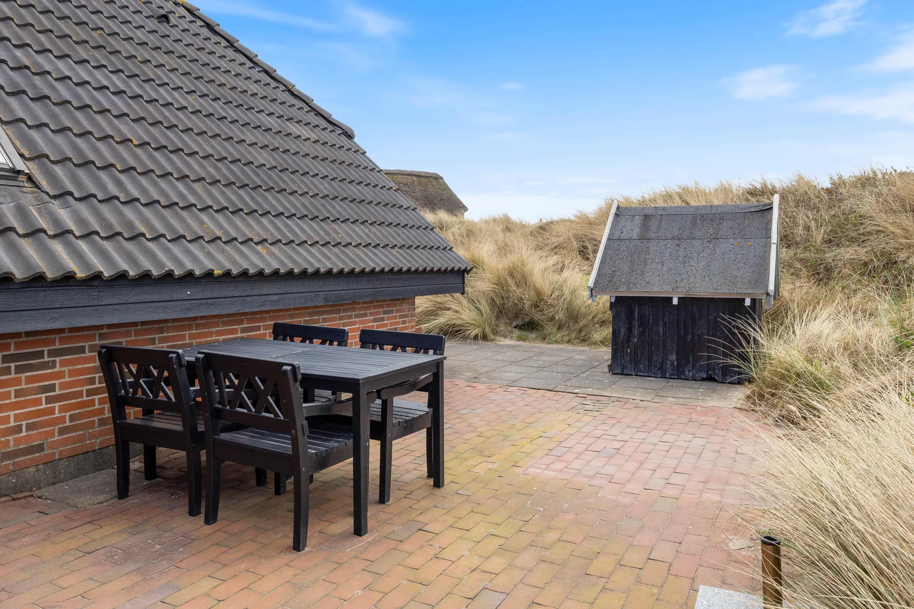 A brick-paved patio beside a brick house, with outdoor seating and a small wooden shed.