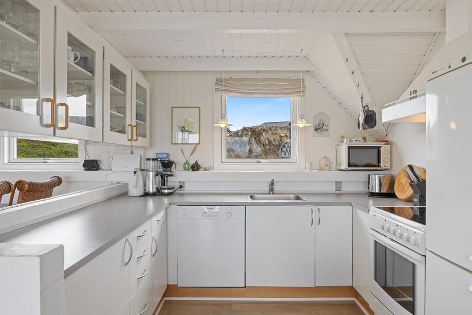 A bright white kitchen with counters, cabinets, and a window overlooking rocky scenery.