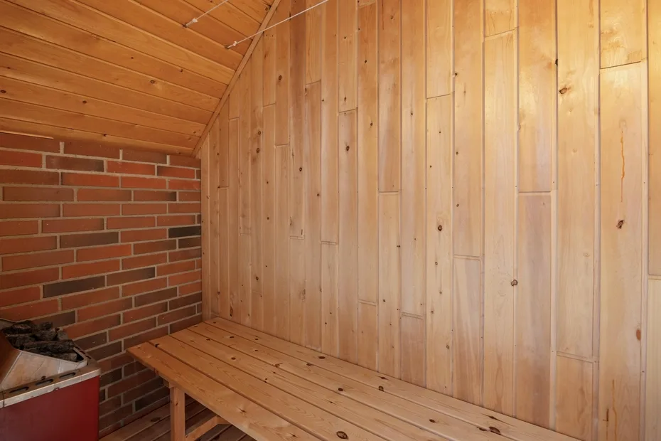 A wood-paneled sauna room with a wooden bench beside a brick wall.