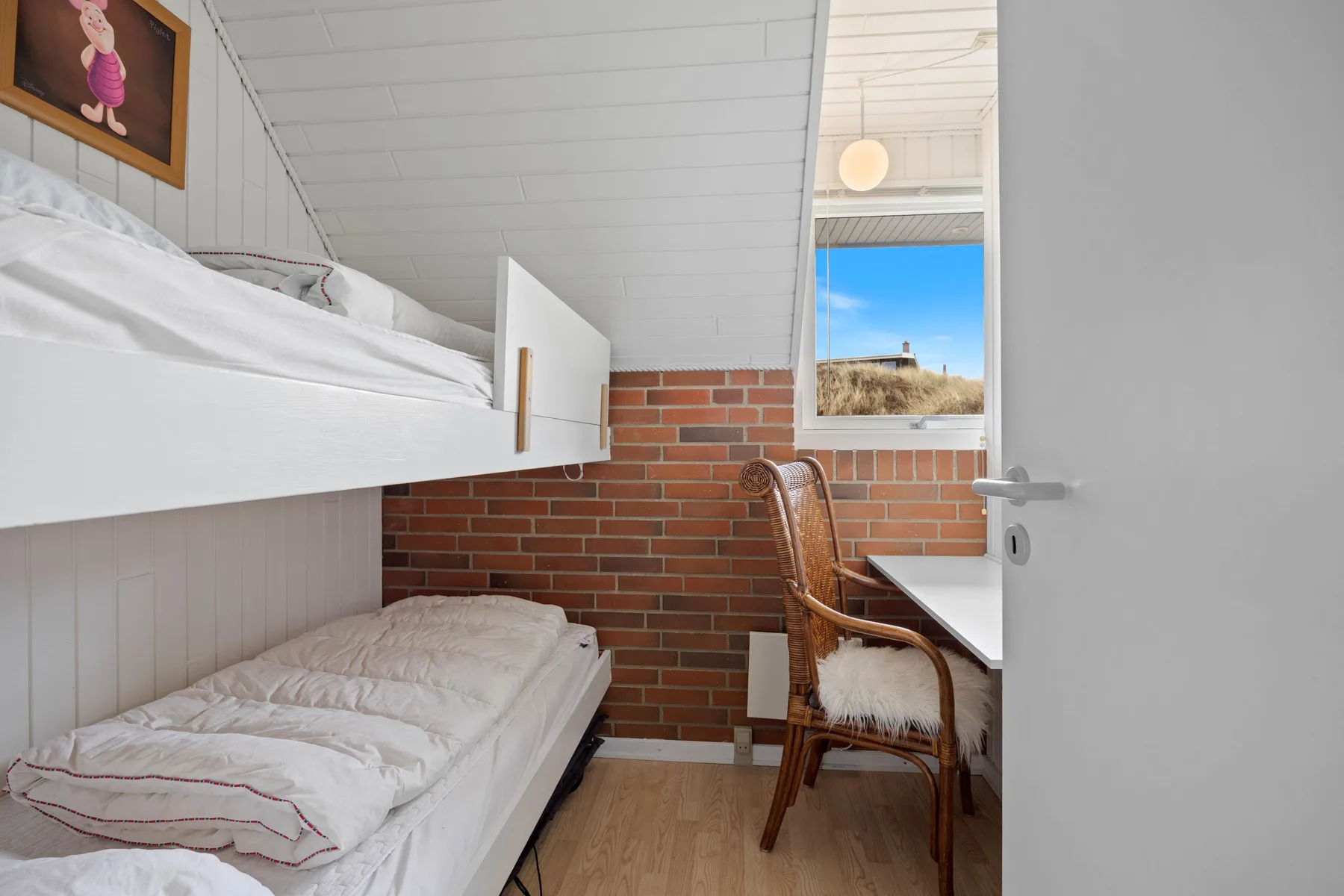 A compact bedroom with bunk beds, brick walls, and a window overlooking the dunes.