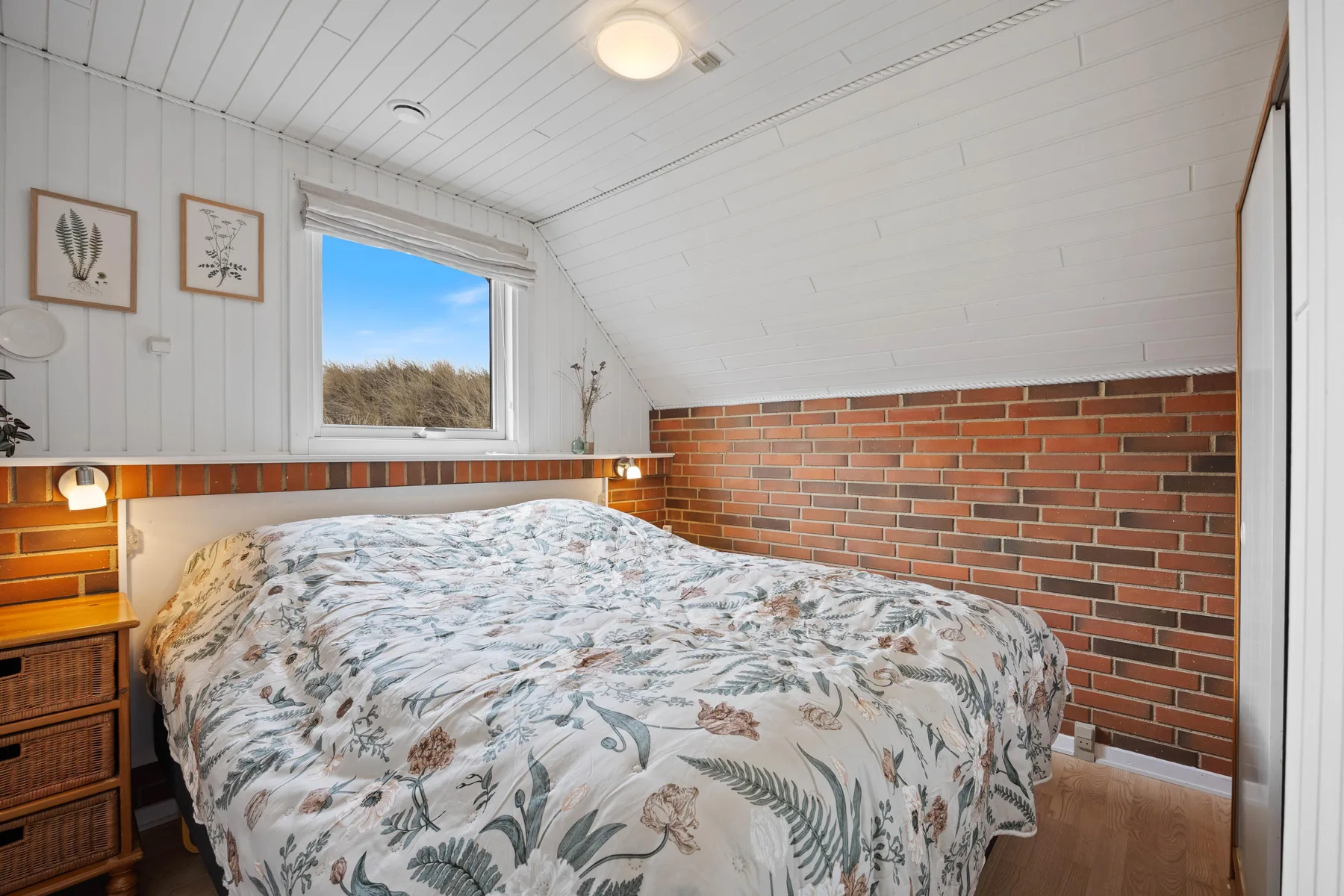 A bedroom with a bed beneath a window and brick-patterned wall.