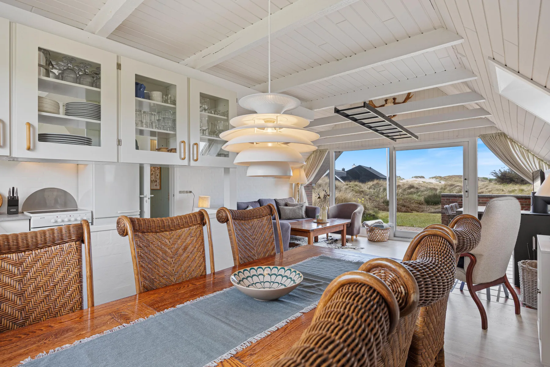 A bright dining area with a long table and windows overlooking the landscape.