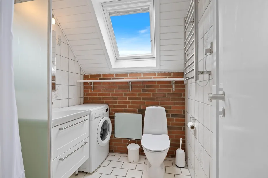 A bright bathroom with a toilet, sink, and skylight.