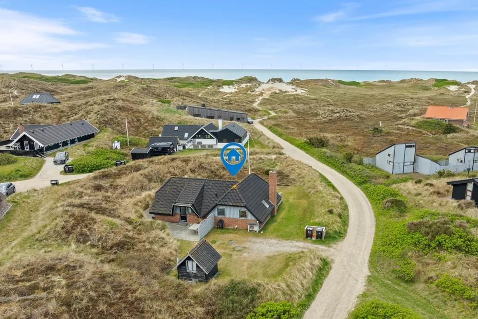 Aerial view of houses along a winding road through coastal dunes.