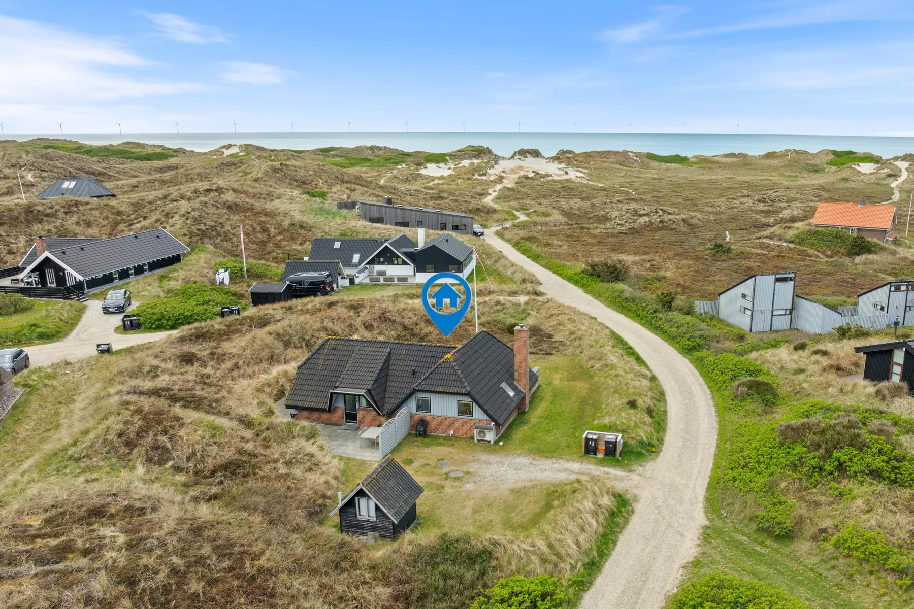 Aerial view of houses among coastal dunes, with the sea on the horizon.