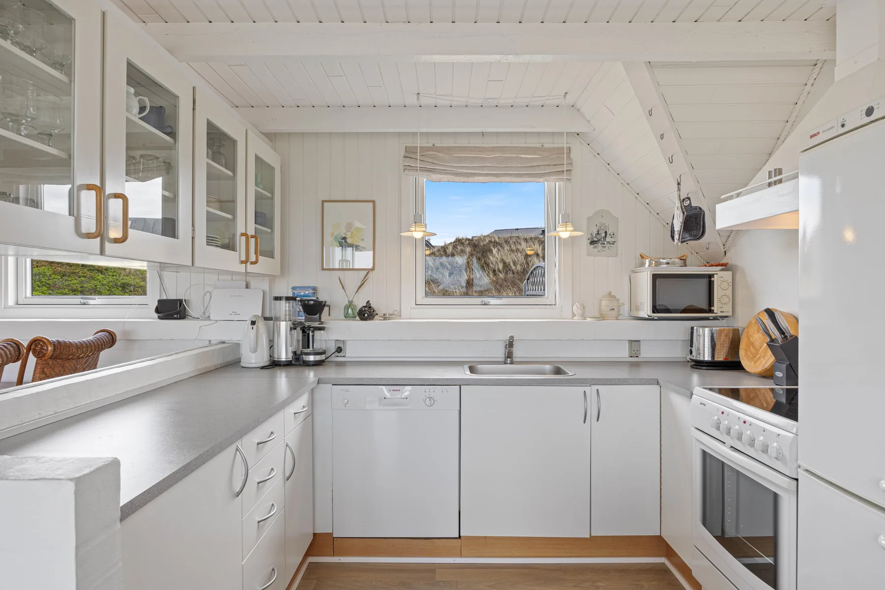 A bright kitchen with white cabinets and a window overlooking the landscape.