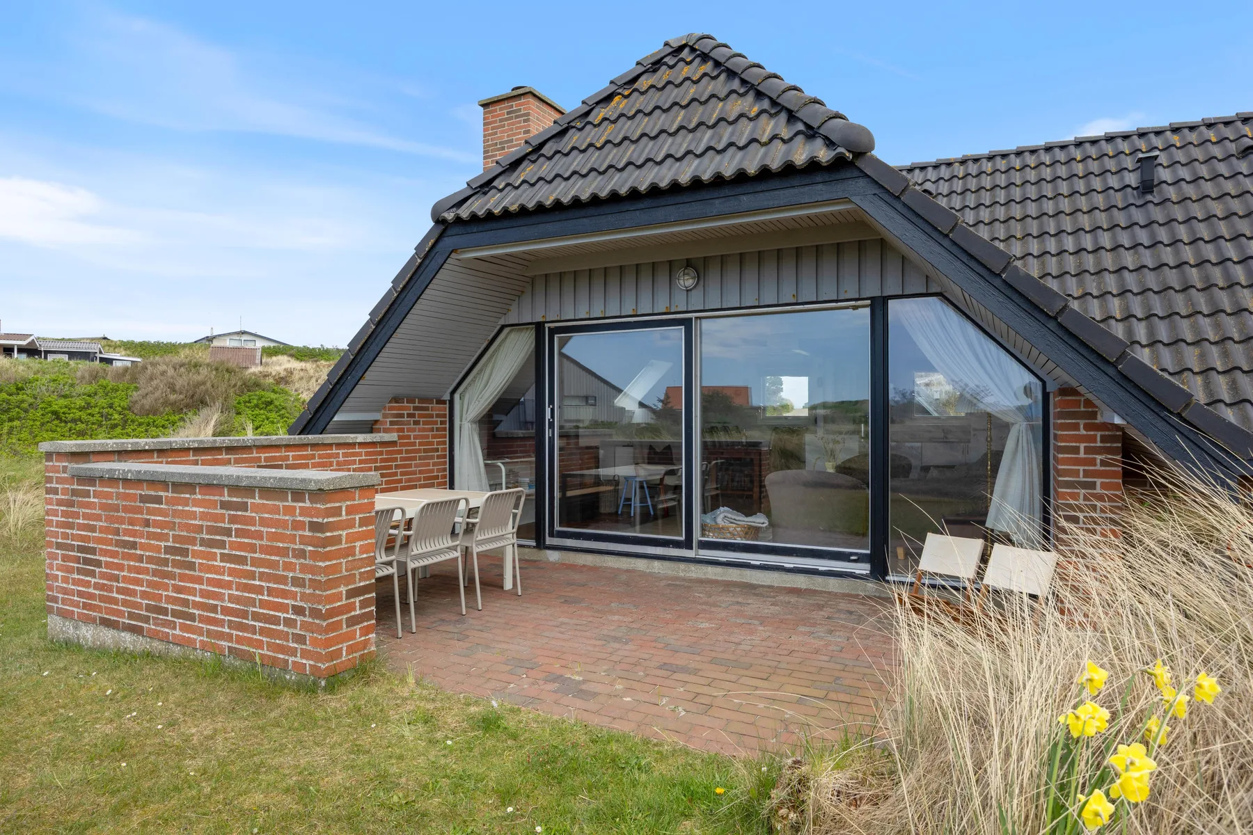 A brick house with large glass doors opens onto a paved patio.