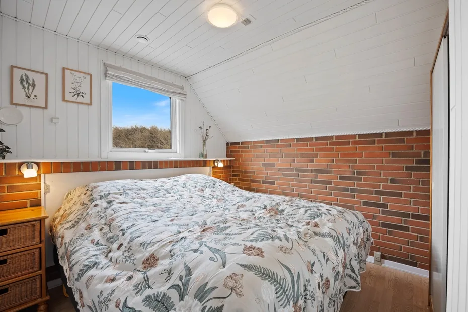 A bedroom with a bed beneath a window and brick wall.